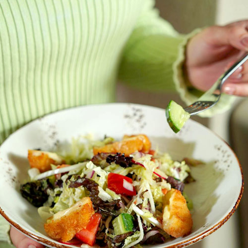 close up of bowl of salad held by a woman in green top